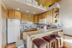 Eine Küche mit Holzausstattung, einem Kühlschrank, einer Mikrowelle, einem Spülbecken und einer Bar mit Barhocker.