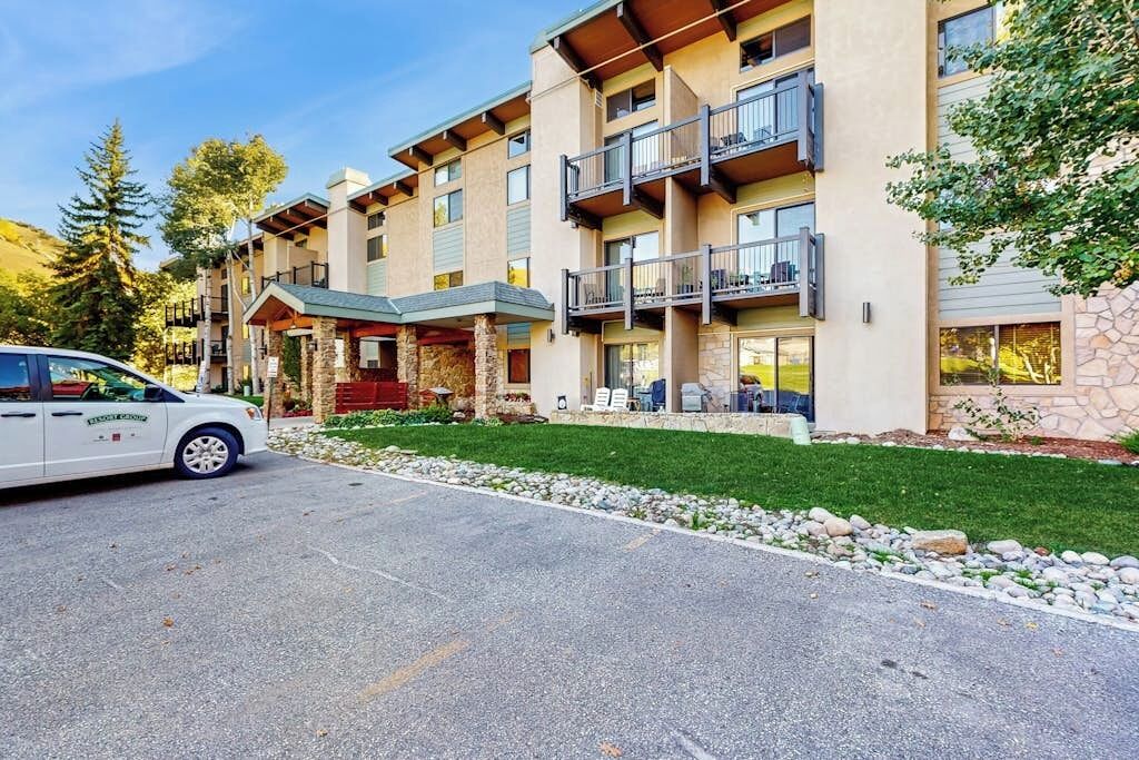 A multi-story hotel with balconies, a parking area, and a well-maintained lawn.
