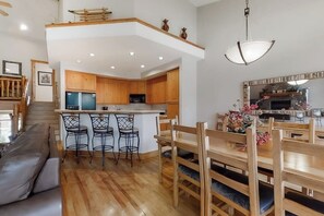 Eine moderne Küche mit Holzausstattung, einer zentralen Kochinsel mit Barhocker und einem Essbereich mit Holztischen und -stühlen.