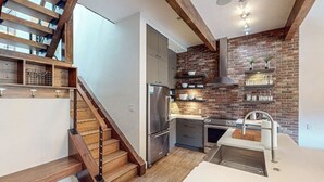 Eine moderne Küche mit Ziegelwand, Edelstahlgeräten und einer Holztreppe.