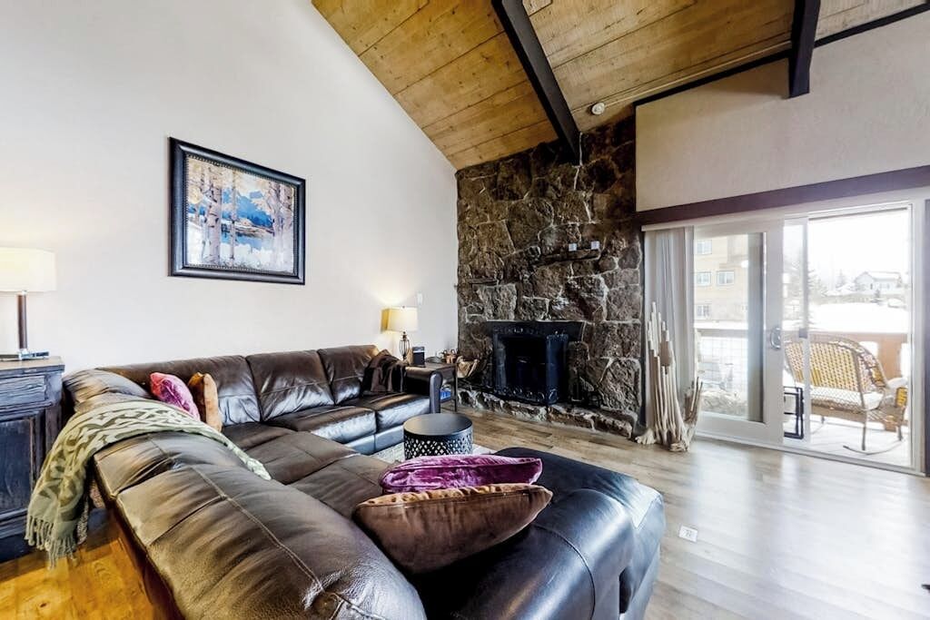A living room with a stone wall, a fireplace, a leather sofa, and a large window.