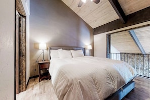 Ein Schlafzimmer mit einem großen Bett, zwei Nachttischlampen, einem Holznachttisch und Blick ins Freie durch ein Fenster.