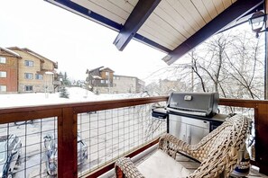 Ein Balkon mit Grill, Korbmöbeln und Blick auf Gebäude und Schnee.