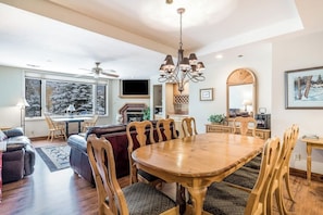 A spacious living area with a wooden dining table, comfortable seating, a fireplace, and large windows. - Second Floor Condo with Shared Pool and Hot Tub, Fast WiFi, and Gas Fireplace (Steamboat Springs)