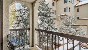 Un balcón con barandilla metálica, una silla y árboles cubiertos de nieve.