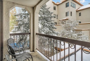 A balcony with a metal railing, a chair, and snow-covered trees. - Second Floor Condo with Shared Pool and Hot Tub, Fast WiFi, and Gas Fireplace (Steamboat Springs)