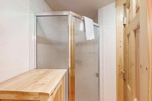 A bathroom with a glass shower enclosure, a wooden bench, and a wooden door. - 2nd-Floor Condo w/Mountain Views, Private Balcony, Fast WiFi, & Gas Fireplace (Steamboat Springs)