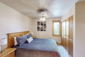 A bedroom with a bed, wooden headboard, bedside tables, a ceiling fan, a window, and a wardrobe. - 2nd-Floor Condo w/Mountain Views, Private Balcony, Fast WiFi, & Gas Fireplace (Steamboat Springs)