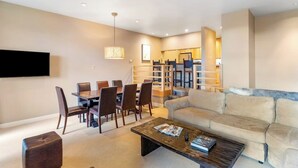 A modern living room with a sofa, coffee table, TV, dining area, and staircase. - Two-story condo with ski view, pool, hot tub & gas fireplace - ski/walk to lifts (Steamboat Springs)