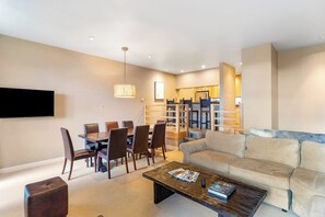 Ein modernes Wohnzimmer mit Sofa, Couchtisch, Fernseher, Essbereich und Treppe.