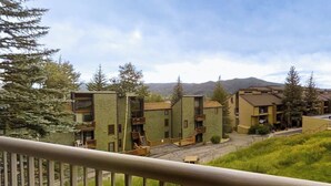 A residential building with multiple balconies, a central courtyard, and a mountainous backdrop. - Two-story condo with ski view, pool, hot tub & gas fireplace - ski/walk to lifts (Steamboat Springs)