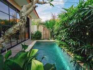 A swimming pool surrounded by lush greenery and a modern building with large windows. - Industrial Luxury Villa – 2BR & Private Pool (Badung)