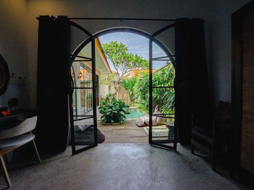 An open doorway leading to a garden with a pool, surrounded by plants and a wooden deck.