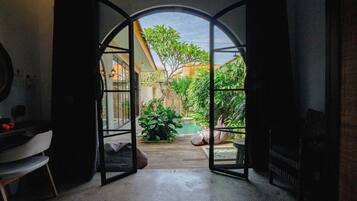 An open doorway leading to a garden with a pool, surrounded by plants and a wooden deck.