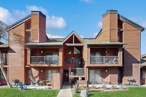 A multi-story building with balconies, a central entrance, and a small outdoor seating area. - Lovely condo with shared pool, sauna, hot tub, tennis, free WiFi, gas fireplace (Steamboat Springs)