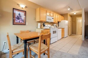 Una cocina con armarios de madera, microondas, refrigerador y una mesa de comedor con sillas.