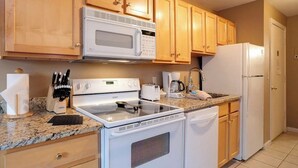 Una cocina con armarios de madera, microondas, estufa, refrigerador y cafetera.