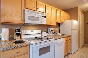 A kitchen with wooden cabinets, a microwave, a stove, a refrigerator, and a coffee maker.