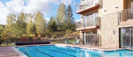 A swimming pool with a stone facade building, outdoor seating, and trees in the background.