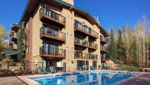 Un hotel de varios pisos con balcones, piscina y un paisaje boscoso de fondo.