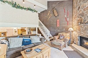 A living room with a fireplace, a staircase, and ski equipment on the wall. - Ski-in/ski-out mountain view condo with gas fireplace, hot tubs, & fitness room (Steamboat Springs)