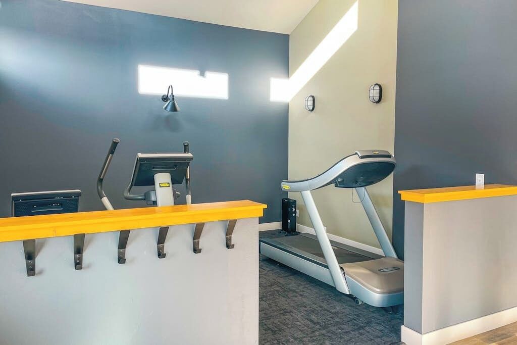 A fitness area with a treadmill, elliptical, and stationary bike, a reception desk, and a wall-mounted light fixture.
