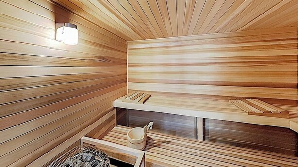 Ein Saunaraum mit Holzlatten, einer Lampe, einer Sitzbank und einem kleinen Ablagebrett.