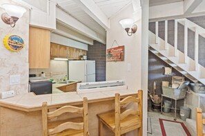 Cozinha com armários de madeira, bancada e luminária pendente.