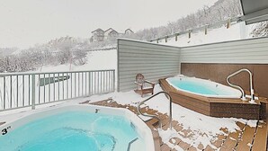 Ein Whirlpool und Schwimmbecken auf einer verschneiten Terrasse mit Blick auf Häuser im Hintergrund.