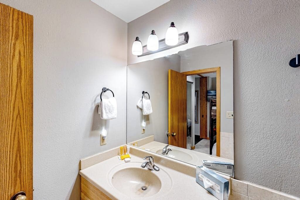 Un baño con lavamanos, espejo, toallero y puerta de madera.