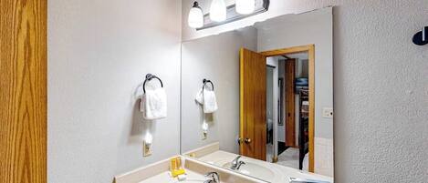 Un baño con lavamanos, espejo, toallero y puerta de madera.