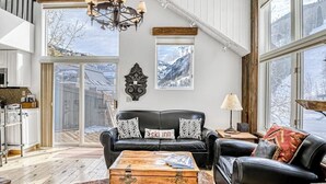 A spacious living area with a black leather sofa, a wooden coffee table, and a large window offering a view of the outdoors. - Charming chalet with fireplace, loft & a true ski-in/out location (Telluride)