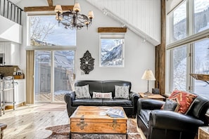 Ein großzügiger Wohnbereich mit einem schwarzen Ledersofa, einem Holztisch und einem großen Fenster mit Blick ins Freie.