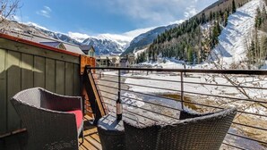 A balcony with wicker chairs, a red umbrella, and a view of snow-covered mountains. - Charming chalet with fireplace, loft & a true ski-in/out location (Telluride)