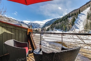 Ein Balkon mit Korbstühlen, einem roten Sonnenschirm und Blick auf schneebedeckte Berge.