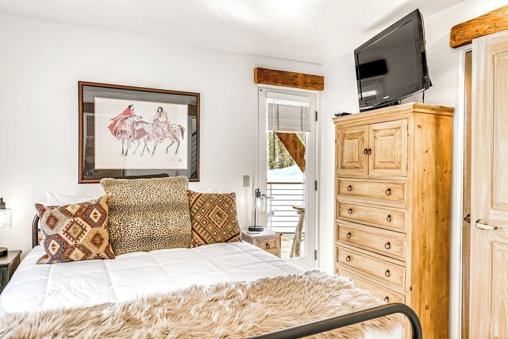 A bedroom with a bed, a wooden dresser, a television, and a framed picture on the wall.
