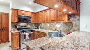 Una cucina con mobili in legno, piani di lavoro in granito, elettrodomestici in acciaio inossidabile e schienale in granito.