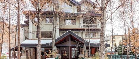 A two-story building with a stone facade, a central entrance with a covered porch, and a balcony on the upper floor.