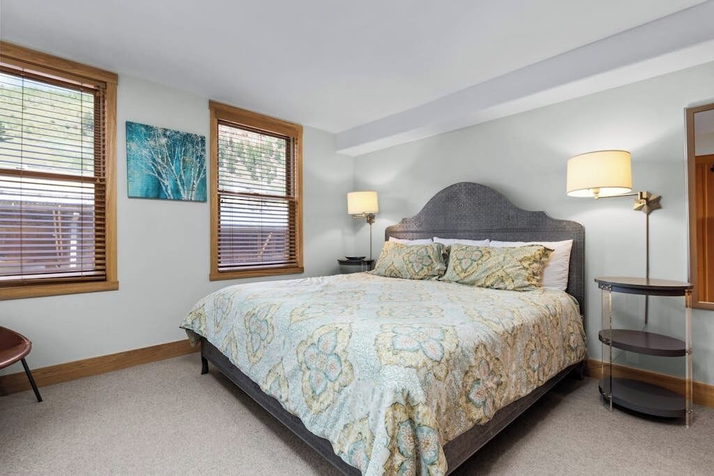 A bedroom with a bed, two bedside lamps, a nightstand, a chair, and a painting on the wall.
