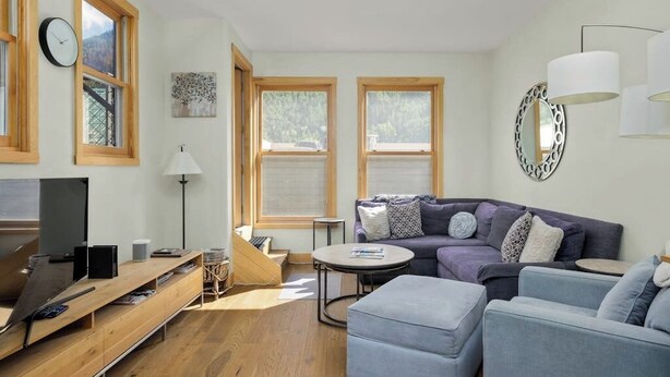 Een moderne woonkamer met een bank, een voetenbankje en een televisie op een houten dressoir.