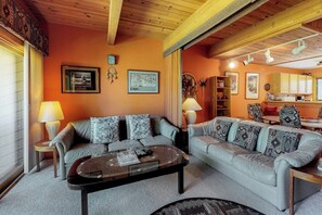 A living room with two sofas, a coffee table, and a kitchen area visible through an open doorway.