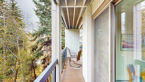 Eine Holzterrasse mit Stuhl, Glastür und Blick auf Bäume.