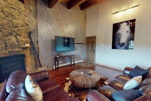 A living room with a stone wall, a fireplace, a mounted TV, a large horse painting, and leather sofas. - Luxury condo w/ full kitchen, balcony, shared pool & hot tub - great location (Steamboat Springs)