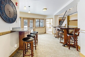 A spacious kitchen with a large clock, bar stools, and a staircase leading to an upper level. - Luxury condo w/ full kitchen, balcony, shared pool & hot tub - great location (Steamboat Springs)