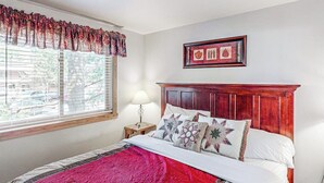 Een slaapkamer met een bed, een raam met zonwering, een nachtkastje met een lamp en een ingelijst schilderij aan de muur.