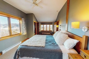 Ein Schlafzimmer mit Bett, Deckenventilator, Blick durch ein Fenster und Nachttisch.
