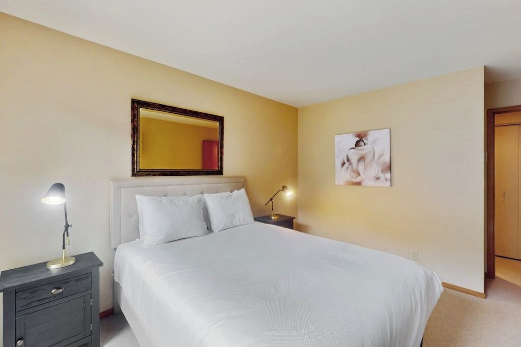 Une chambre d’hôtel comprenant un lit, des tables de chevet, une commode, un miroir et un tableau accroché au mur.