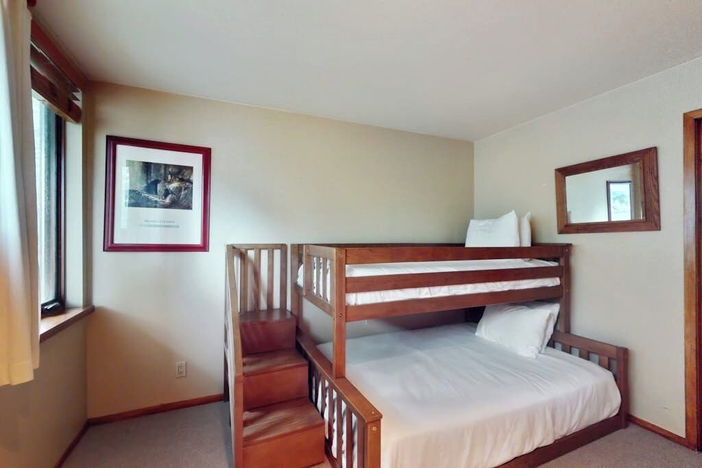 A bunk bed room with a framed picture on the wall, a window with curtains, and a mirror on the wall.