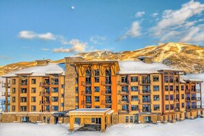 Ein mehrstöckiges Hotel mit Balkonen, einer überdachten Außenlounge und einer Bergkulisse im Hintergrund.