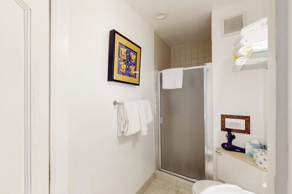 Un baño con ducha, inodoro, lavabo y un cuadro en la pared.